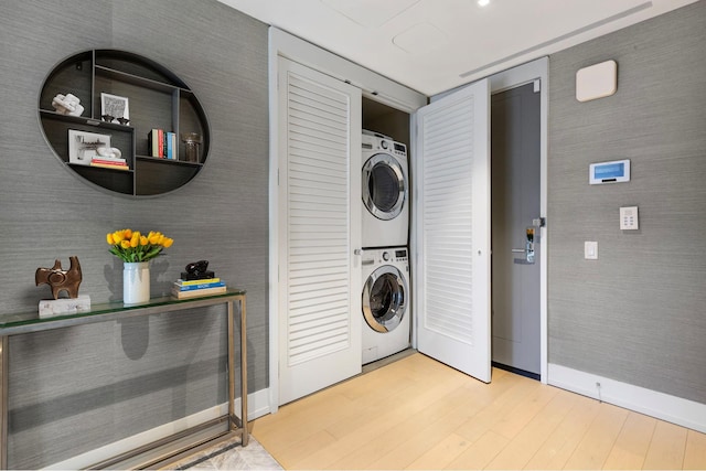 washroom with stacked washer / dryer, wood finished floors, laundry area, baseboards, and wallpapered walls