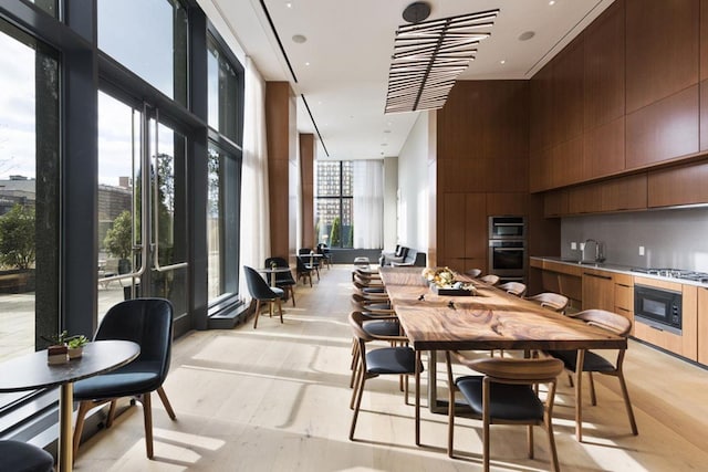 dining space with a towering ceiling, light wood-style flooring, and expansive windows