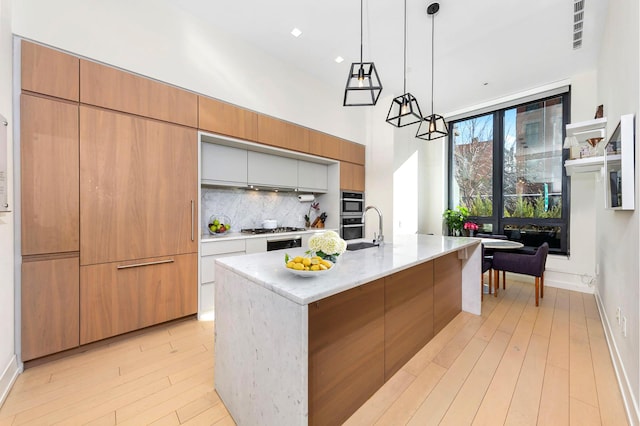 kitchen featuring light wood-style flooring, stainless steel gas cooktop, a high ceiling, a sink, and tasteful backsplash