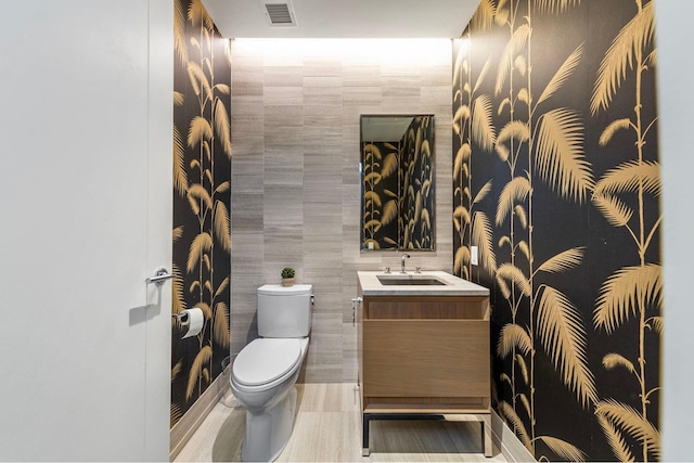 half bathroom featuring toilet, vanity, visible vents, and tile walls