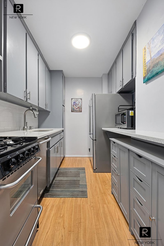 kitchen featuring light wood finished floors, stainless steel appliances, gray cabinets, light countertops, and a sink