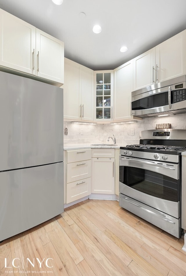 kitchen featuring light wood finished floors, a sink, stainless steel appliances, light countertops, and decorative backsplash