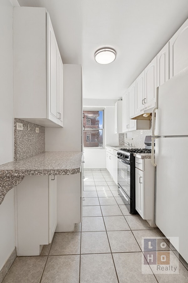 kitchen with range with gas cooktop, light tile patterned floors, tasteful backsplash, freestanding refrigerator, and white cabinetry