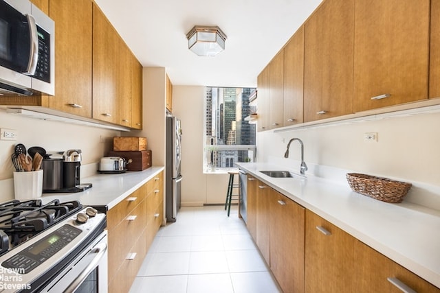 kitchen featuring appliances with stainless steel finishes, brown cabinetry, light countertops, and a sink