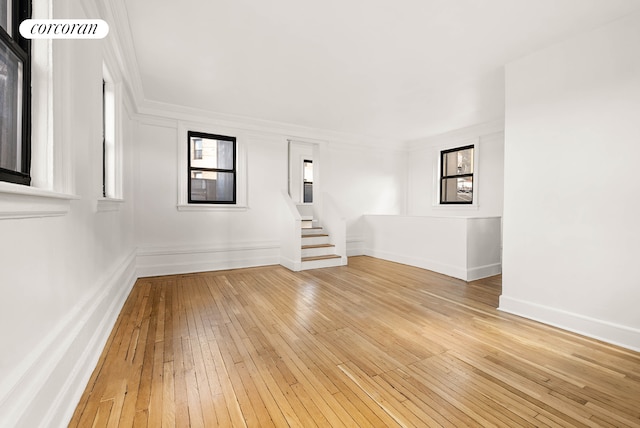 empty room featuring baseboards, crown molding, stairway, and light wood-style floors