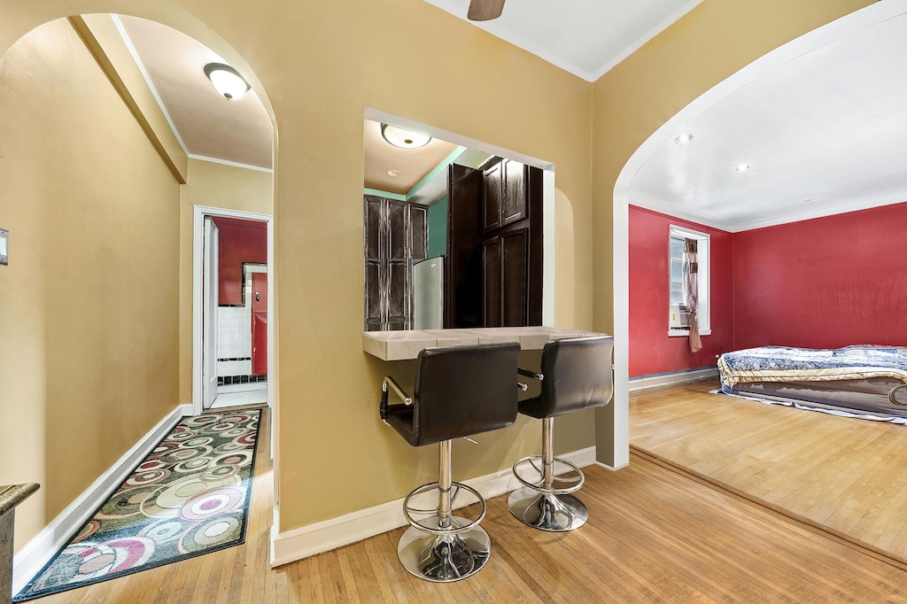 kitchen featuring arched walkways, wood finished floors, ornamental molding, baseboards, and freestanding refrigerator