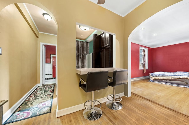 kitchen featuring arched walkways, wood finished floors, ornamental molding, baseboards, and freestanding refrigerator