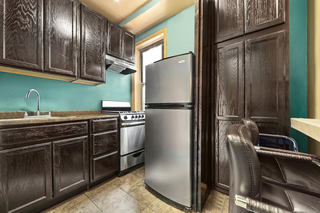 kitchen with appliances with stainless steel finishes, under cabinet range hood, a sink, and dark brown cabinets