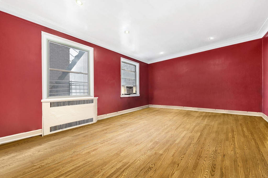 unfurnished room with radiator heating unit, wood finished floors, baseboards, crown molding, and cooling unit