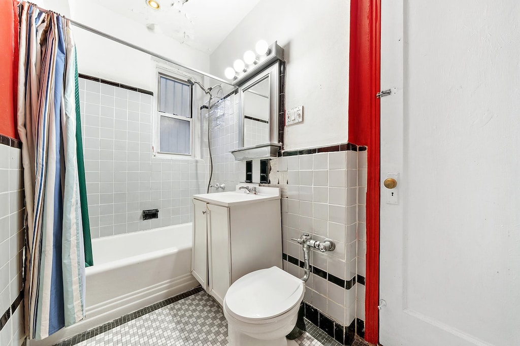 full bath with wainscoting, toilet, shower / bath combination with curtain, vanity, and tile walls