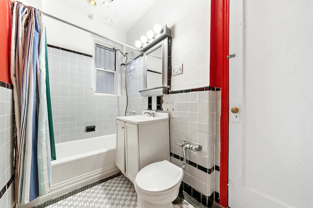 bathroom featuring tile walls, shower / bath combo, vanity, toilet, and a wainscoted wall
