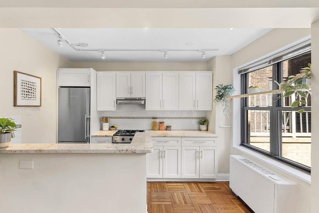 kitchen with stainless steel fridge, white cabinets, range, radiator, and under cabinet range hood