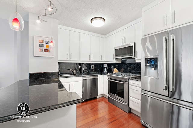 kitchen with tasteful backsplash, stainless steel appliances, wood finished floors, white cabinetry, and a sink