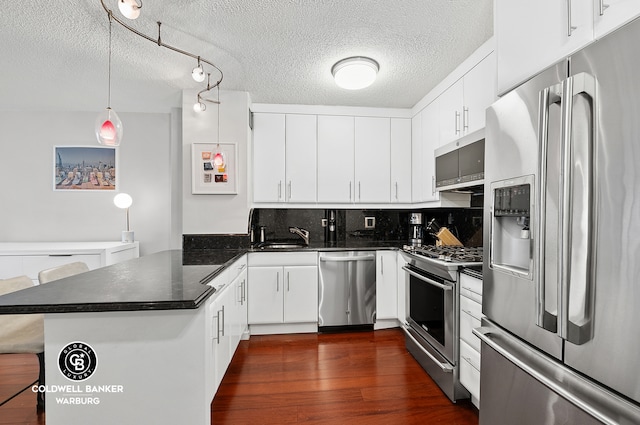 kitchen featuring dark wood-style floors, stainless steel appliances, decorative backsplash, white cabinets, and a peninsula