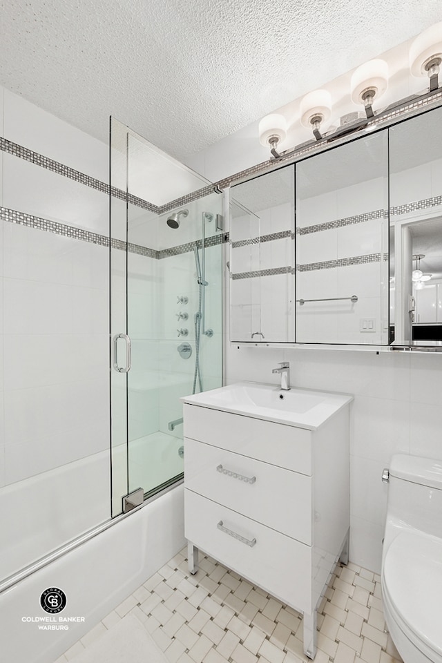 bathroom featuring toilet, combined bath / shower with glass door, a textured ceiling, and vanity