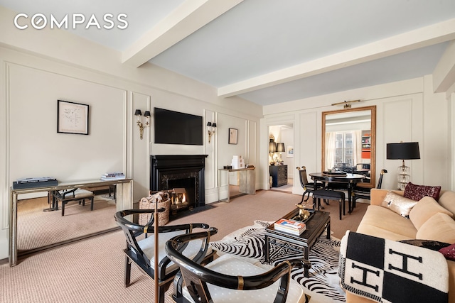 living area with beamed ceiling, a fireplace with flush hearth, light colored carpet, and a decorative wall