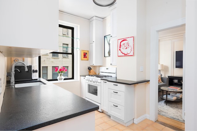 kitchen with light tile patterned floors, dark countertops, white cabinets, a sink, and white range with gas stovetop