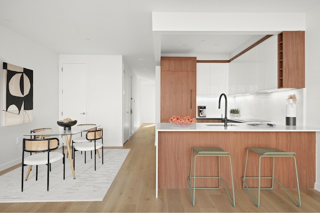 kitchen featuring light wood finished floors, a kitchen bar, light countertops, modern cabinets, and a sink