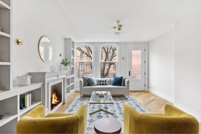 living area with visible vents, a warm lit fireplace, baseboards, and wood finished floors