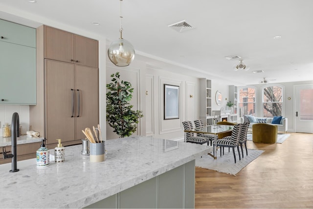 kitchen with decorative light fixtures, light wood finished floors, visible vents, open floor plan, and light stone countertops