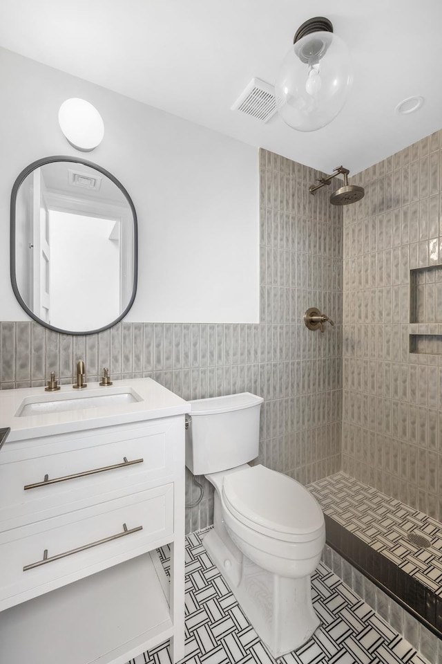 full bath with tile walls, toilet, vanity, tiled shower, and tile patterned floors