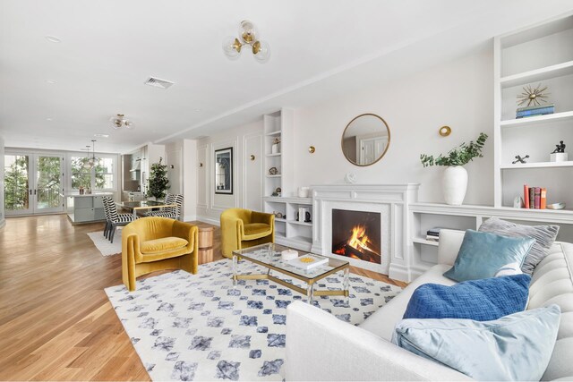 living room featuring a warm lit fireplace, visible vents, baseboards, and wood finished floors