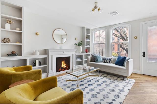 living area featuring plenty of natural light, built in shelves, visible vents, and light wood-style flooring