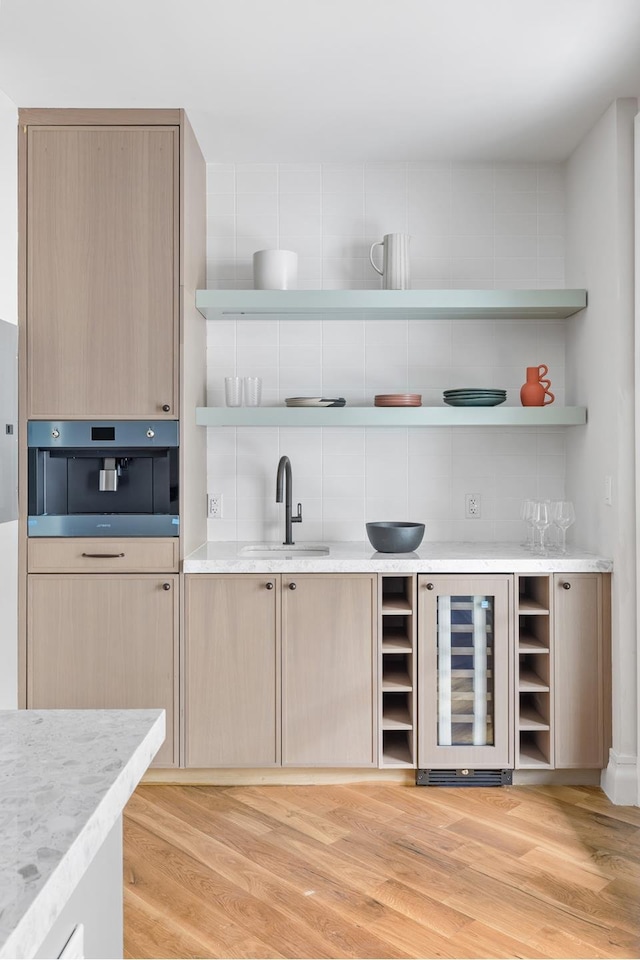 bar with wine cooler, light wood-style flooring, a sink, stainless steel oven, and backsplash