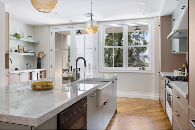 kitchen featuring under cabinet range hood, a spacious island, baseboards, light wood finished floors, and decorative light fixtures