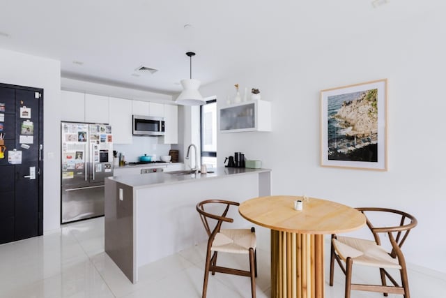 kitchen featuring white cabinets, appliances with stainless steel finishes, decorative light fixtures, a peninsula, and a sink