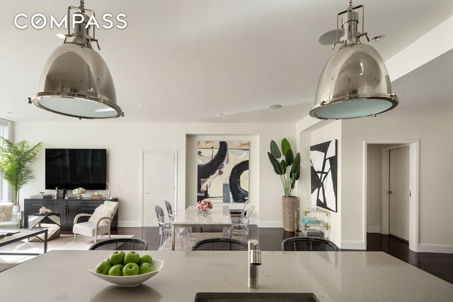 interior space with dark wood-style floors, pendant lighting, open floor plan, a sink, and baseboards