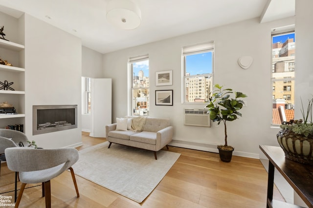 sitting room featuring baseboards, built in features, a wall mounted air conditioner, light wood-style floors, and a fireplace