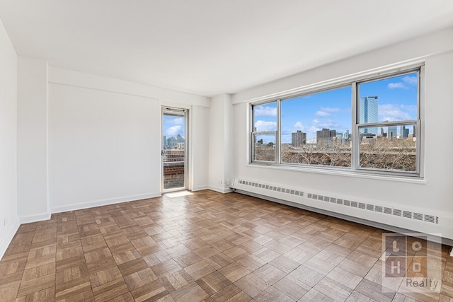 spare room featuring a baseboard radiator, baseboards, and a view of city