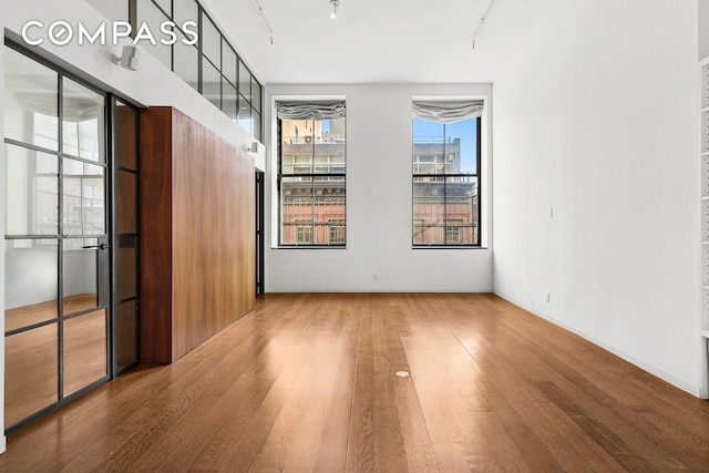 spare room with wood finished floors, rail lighting, and baseboards