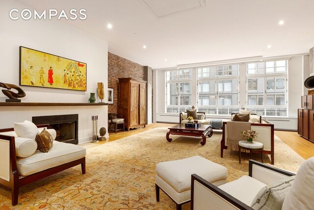 sitting room featuring a fireplace with raised hearth, brick wall, light wood-style flooring, and recessed lighting