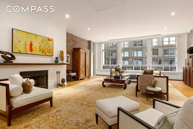 living area with recessed lighting, a fireplace with raised hearth, brick wall, and light wood-style floors