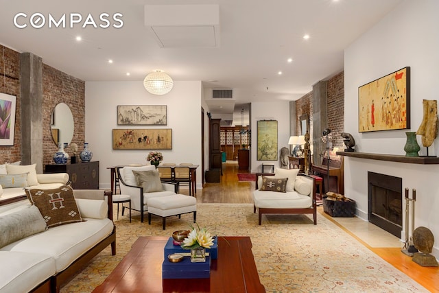 living room with visible vents, a fireplace with flush hearth, wood finished floors, recessed lighting, and brick wall