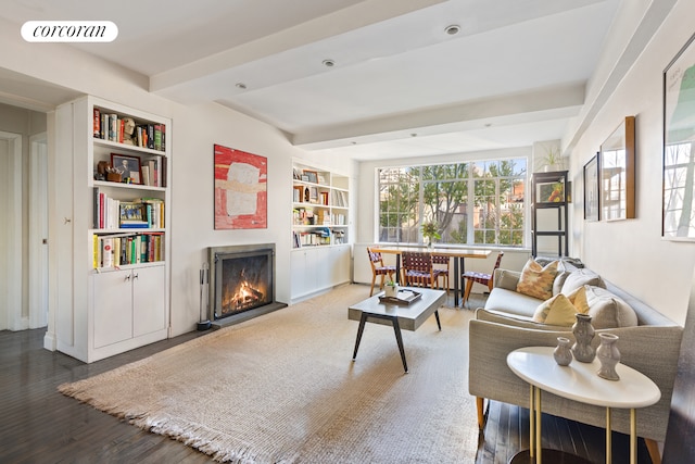 living room with visible vents, built in shelves, beam ceiling, a warm lit fireplace, and wood finished floors