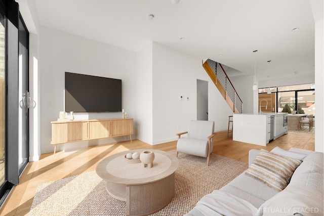 living area with stairs, light wood-type flooring, and baseboards