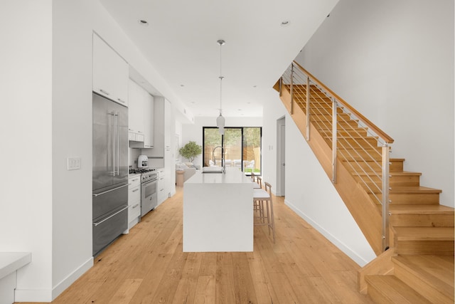 kitchen with light wood-style flooring, high quality appliances, hanging light fixtures, a kitchen island with sink, and white cabinetry