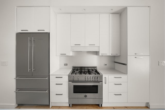 kitchen with light countertops, premium appliances, ventilation hood, and white cabinetry