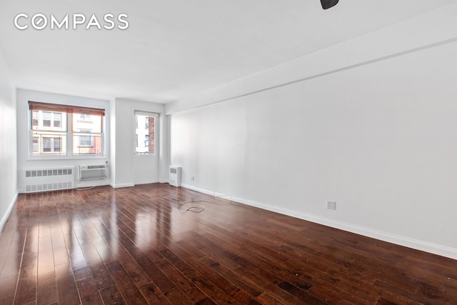 unfurnished room featuring wood-type flooring, baseboards, a wall unit AC, and radiator heating unit