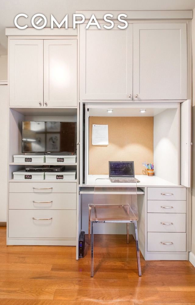 kitchen with light wood finished floors, white cabinets, built in study area, and light countertops