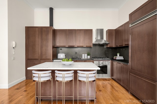 kitchen featuring a kitchen island, stainless steel appliances, crown molding, wall chimney range hood, and a sink