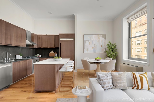 kitchen with a kitchen breakfast bar, a center island, stainless steel appliances, wall chimney range hood, and a sink