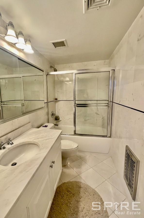 bathroom with enclosed tub / shower combo, tile patterned flooring, visible vents, and vanity