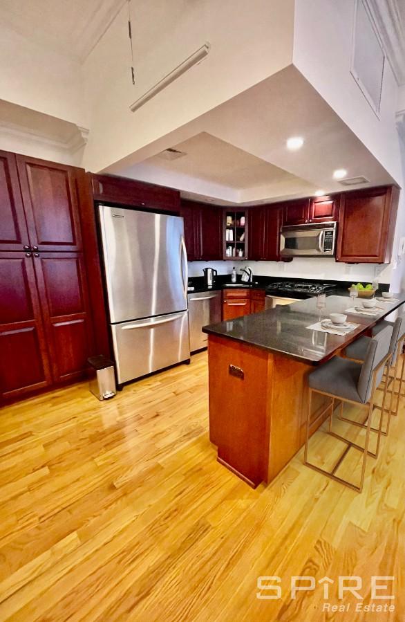 kitchen featuring stainless steel appliances, a peninsula, dark brown cabinets, light wood finished floors, and dark countertops