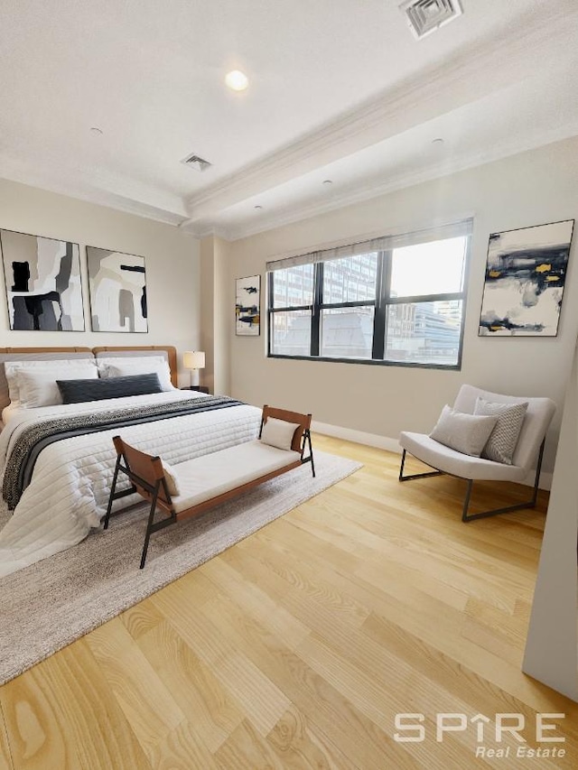 bedroom with crown molding, a raised ceiling, visible vents, light wood-style flooring, and baseboards