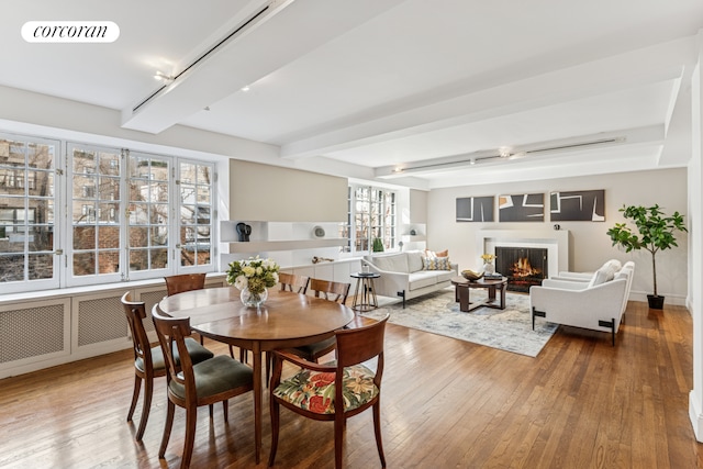 dining room with beamed ceiling, visible vents, hardwood / wood-style floors, and a warm lit fireplace