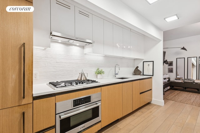 kitchen with stainless steel appliances, backsplash, light wood-style floors, a sink, and under cabinet range hood